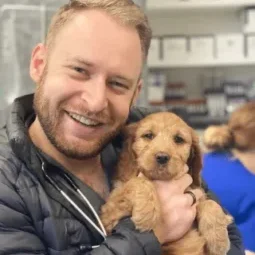Dr Tyler Baum posing for a picture with a small fluffy puppy